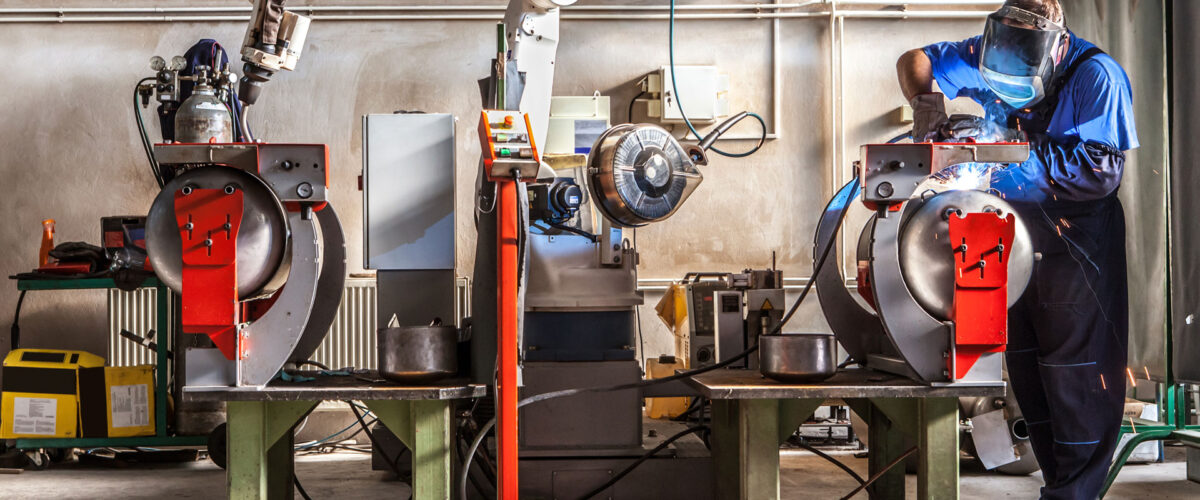 The mechanical performs welds metal components assisted by a worker.