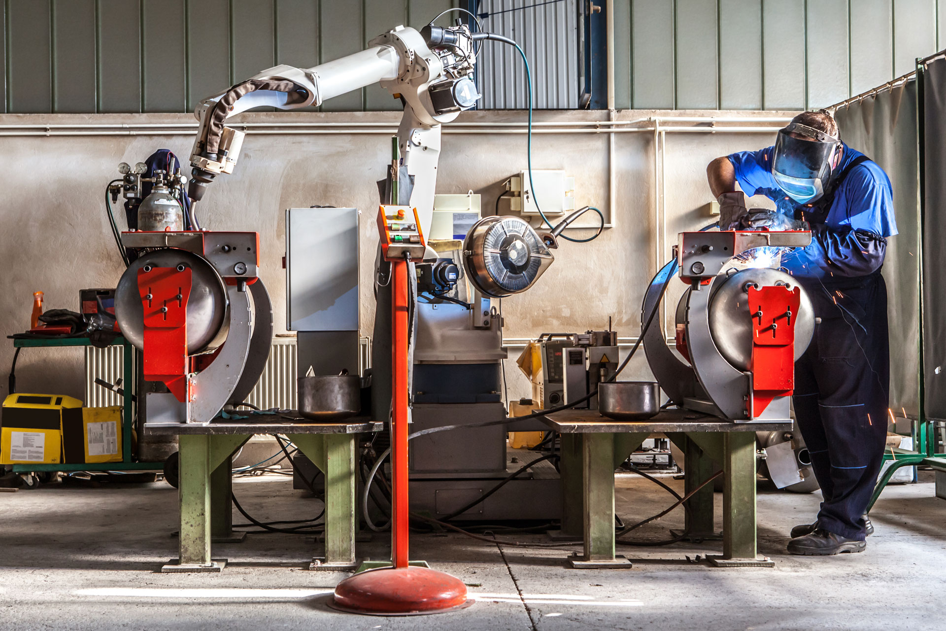 The mechanical performs welds metal components assisted by a worker.